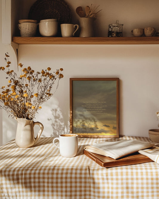 Cozy home setting with a table, mug, open book, and framed Lamentations 3:24-26 Scripture art print on a checkered tablecloth.