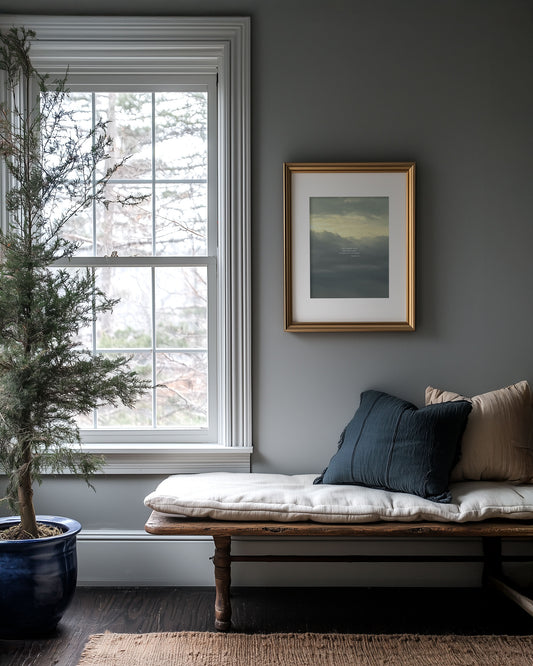 Living room with a window, plant, bench, and framed Matthew 6:10 Scripture art print on a gray wall.