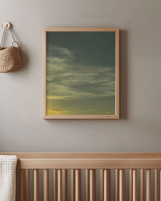 Framed Scripture art print with Psalm 143:8 on top of a wispy cloud sunset sky hanging above a crib in a room.