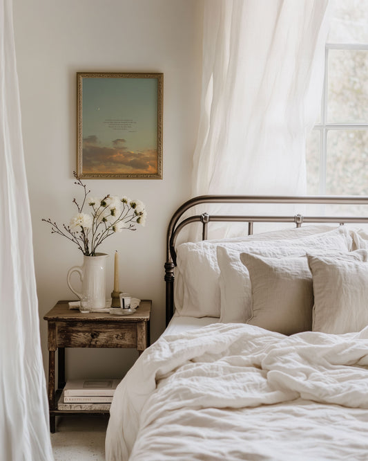 Framed Scripture art print of Psalm 16:7-8 on a blue sunset sky with soft golden/orange clouds and a crescent moon at the top left. The print is hanging on a wall in a cozy bedroom with a bed, nightstand and soft sunlight coming through a window behind the bed to the right of the image.