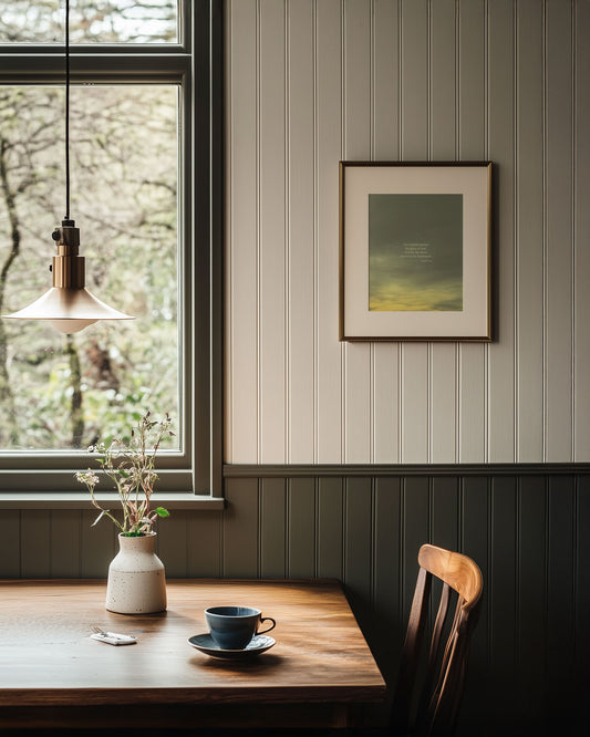 Nest cafe interior with a table, chair, and a framed Scripture art print of Psalm 19:1 with a painting-like sky. The print is hanging on a white paneled wall.