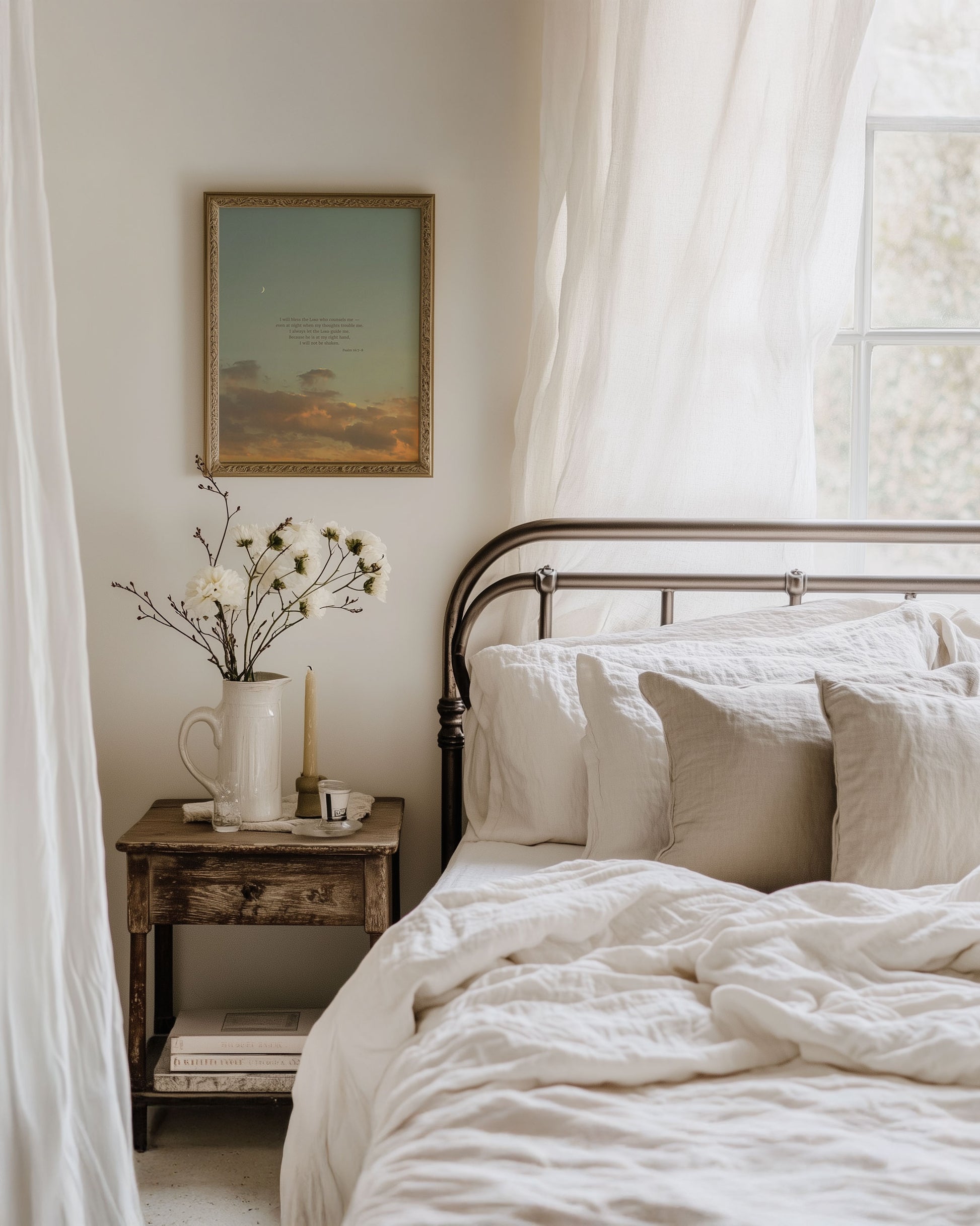 Framed Scripture art print of Psalm 16:7-8 on a blue sunset sky with soft golden/orange clouds and a crescent moon at the top left. The print is hanging on a wall in a cozy bedroom with a bed, nightstand and soft sunlight coming through a window behind the bed to the right of the image.